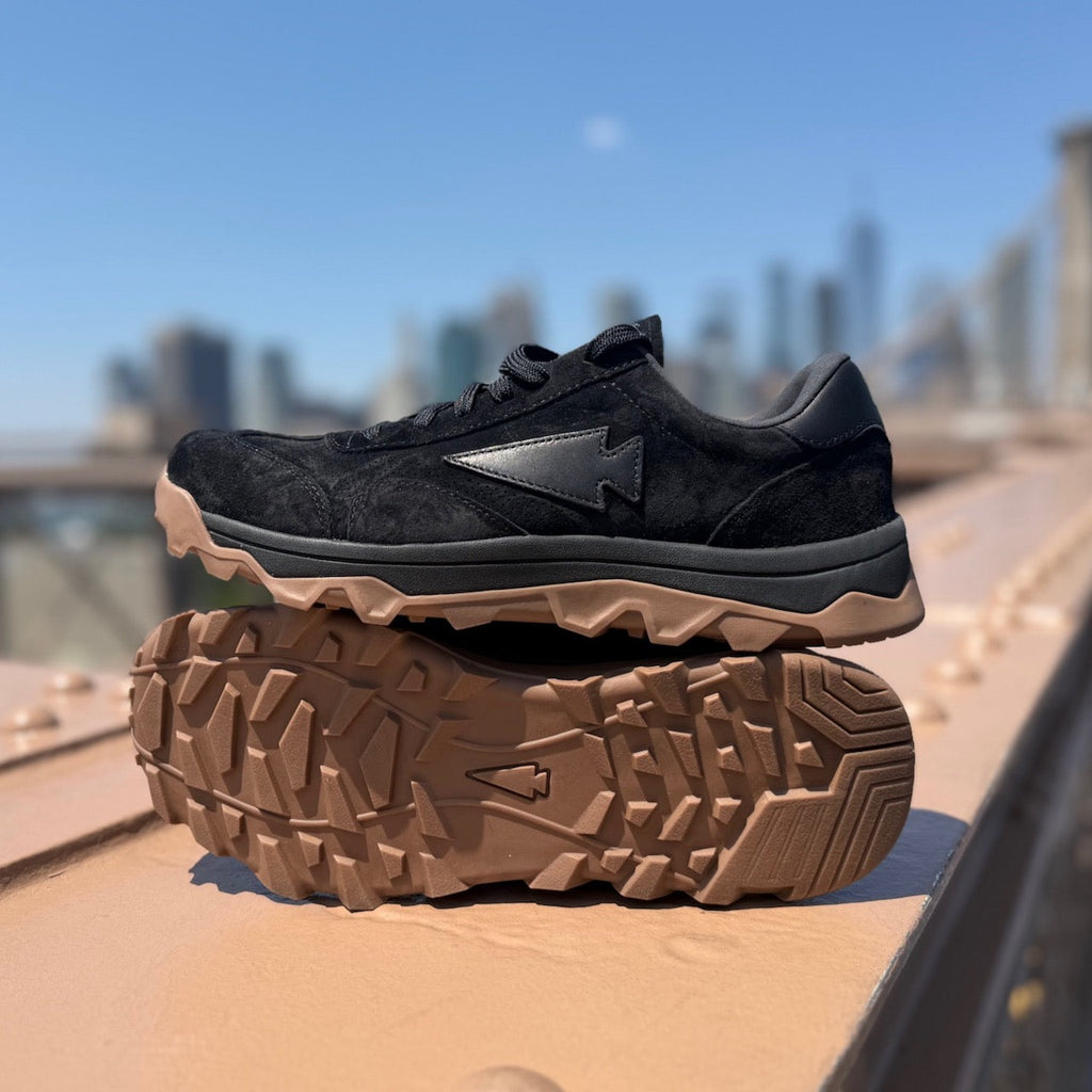 Pair of Mackall 45 Black + Gum shoes displayed outdoors against a city skyline