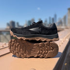 Pair of Mackall 45 Black + Gum shoes displayed outdoors against a city skyline
