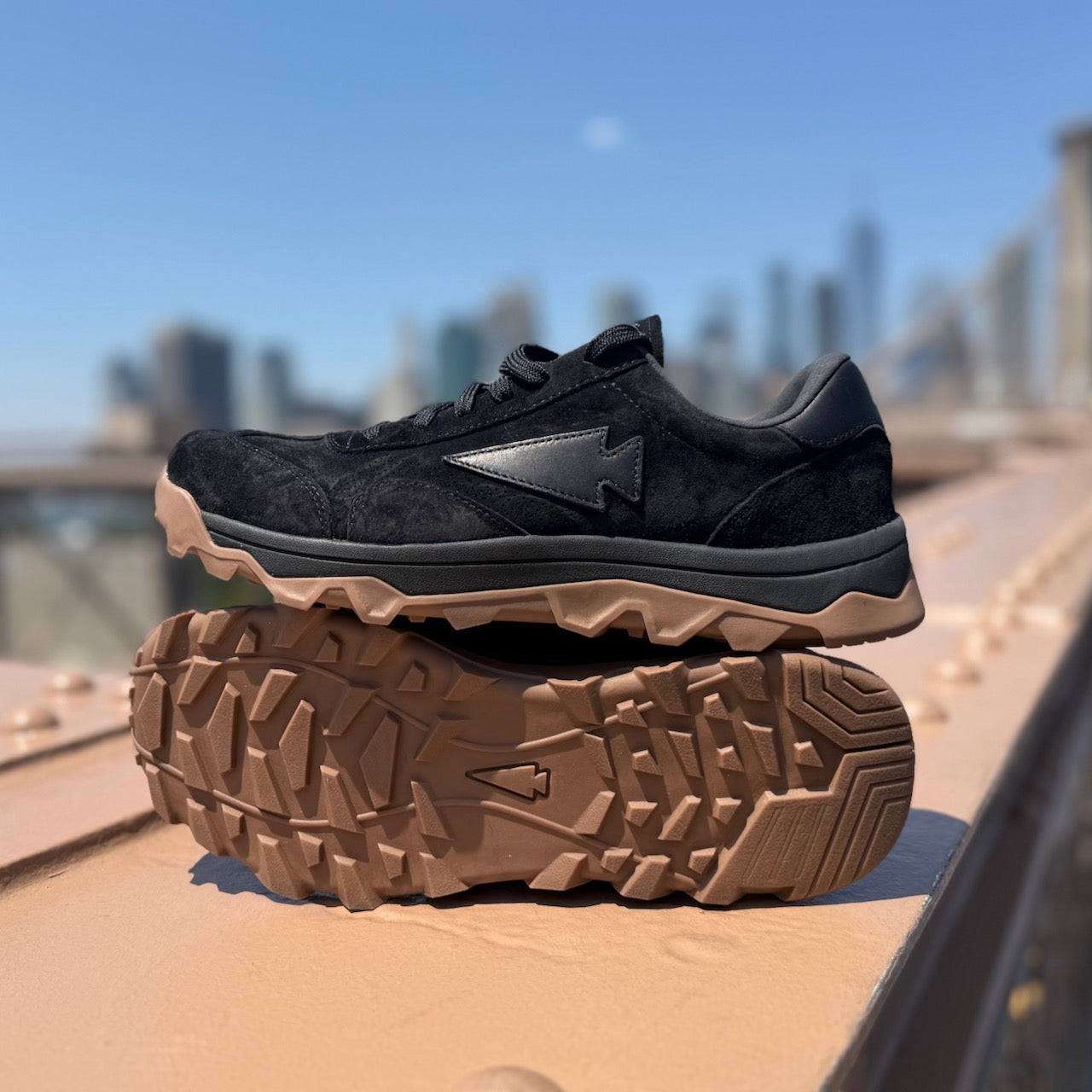 Pair of Mackall 45 Black + Gum shoes displayed outdoors against a city skyline