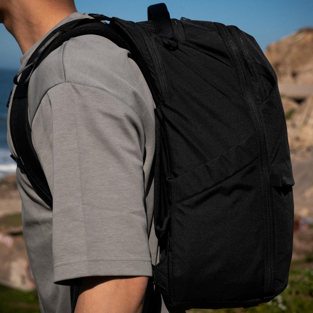 Person wearing a black backpack outdoors with a scenic background