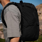 Person wearing a black backpack outdoors with a scenic background